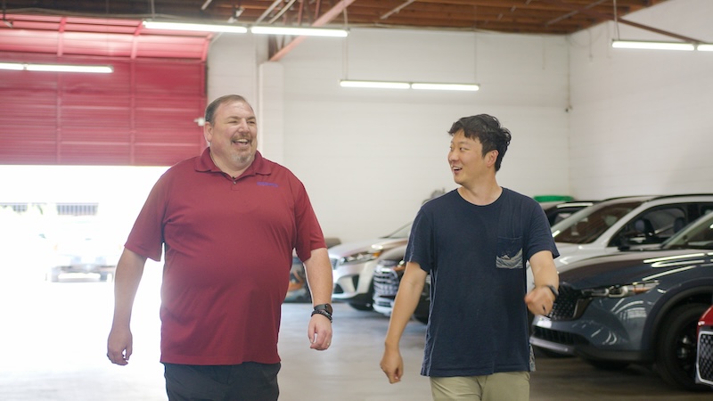 Car broker laughing with client in automobile showroom.